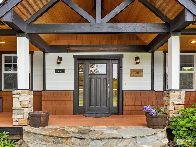 The front entry with timber truss ceiling, stone column bases, and a dark wood craftsman door over a flagstone landing.