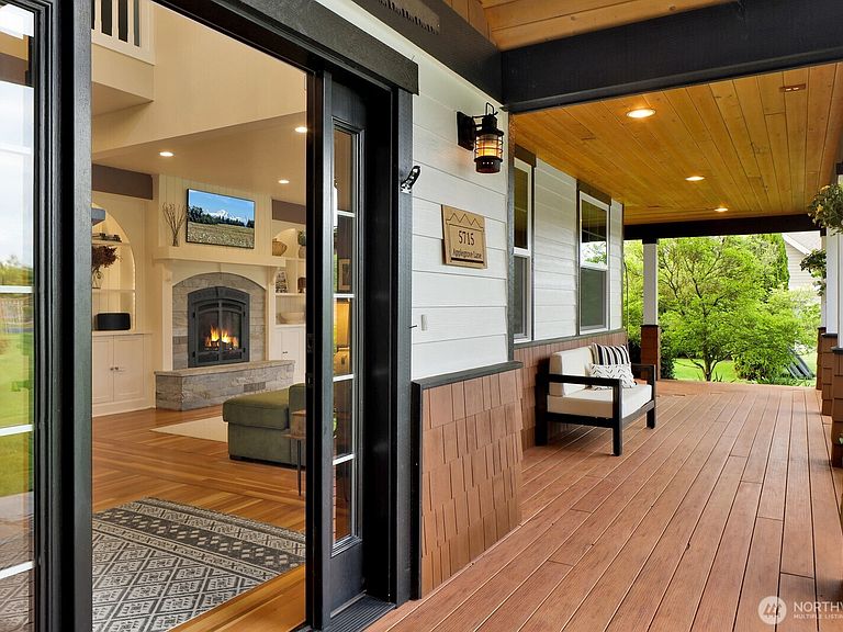 A covered porch with cedar-plank ceiling, hardwood deck, and a sliding glass door looking into the great room with a stone fireplace.